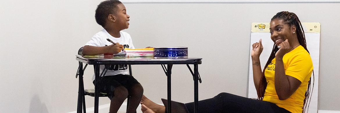 Mom smiling and talking to her young son who is sitting at a small desk