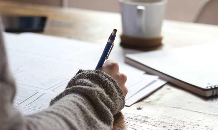 Someone taking notes with a coffee cup sitting on the table next to papers